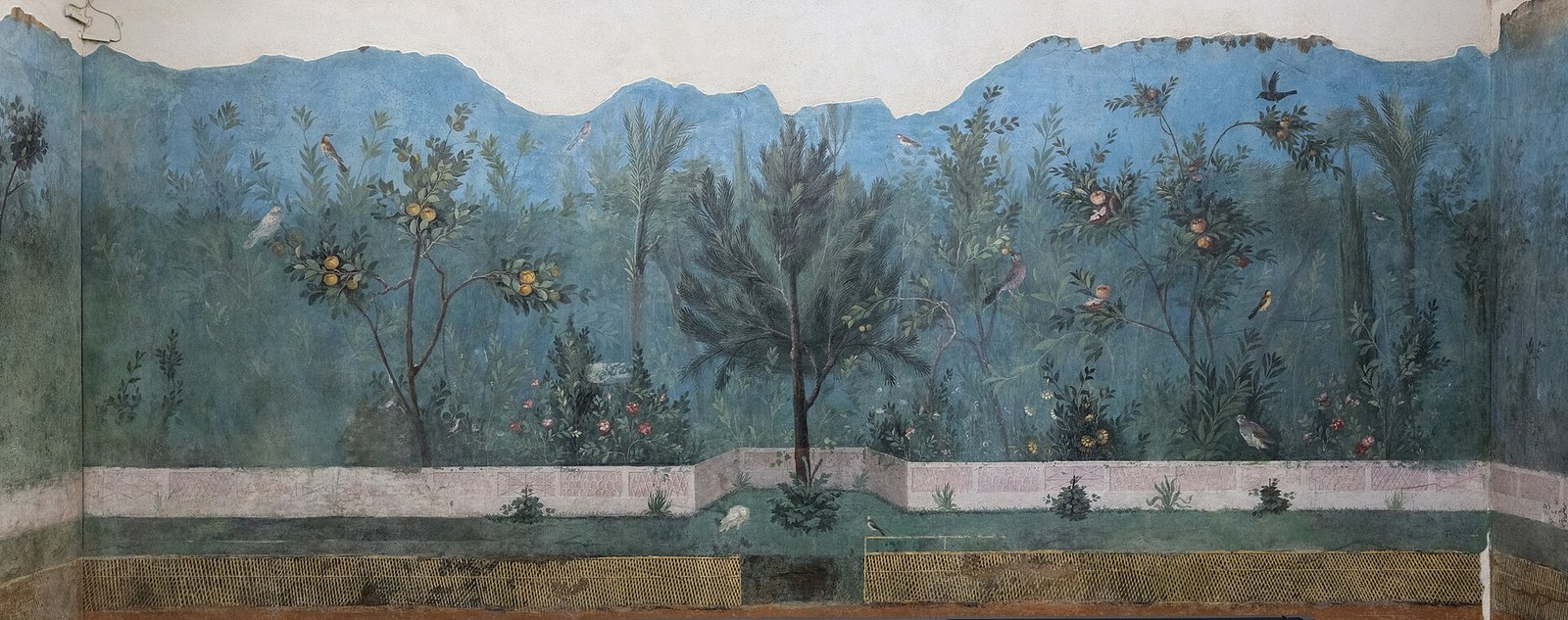 The garden room fresco from the Villa of Livia, now in the Palazzo Massimo in Rome: a painted marble balustrade along the bottom, a strip of lawn with small plants, dense green trees and shrubs carrying ripe fruit with birds perched among them, and behind the planting a pale blue band of hazy distance under a light sky.