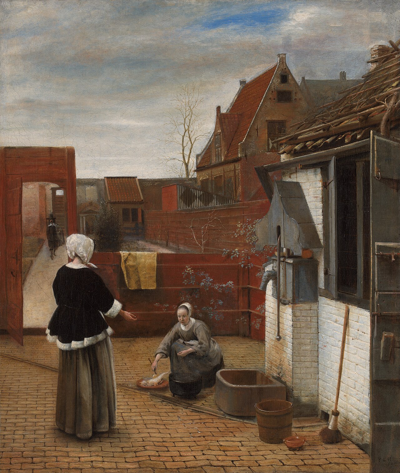 Pieter de Hooch's courtyard scene: a woman in a black jacket trimmed with white fur stands on a brick path while a maid kneels over a cooking pot and a platter of fish, with a water pump, broom and buckets along a whitewashed wall at the right.