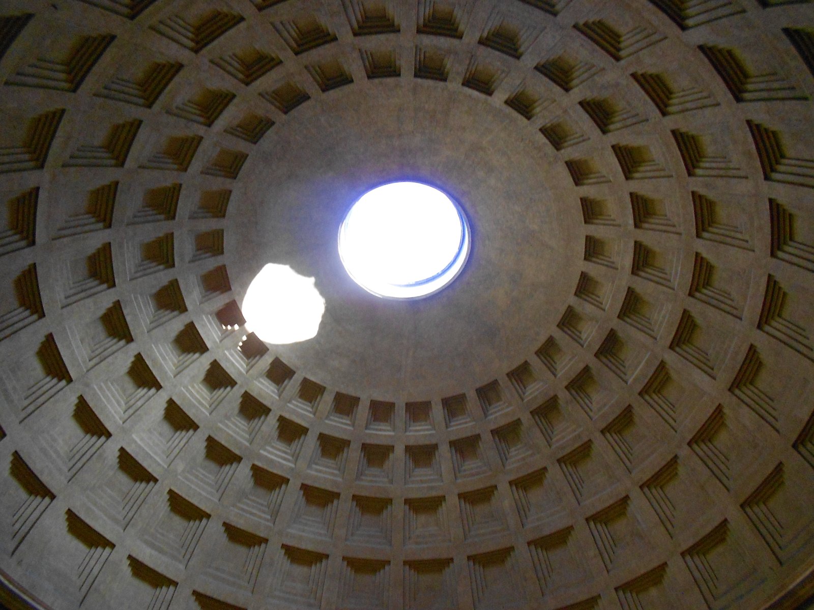 The open oculus and recessed coffers of the Pantheon dome, with a patch of sunlight on the curved surface.