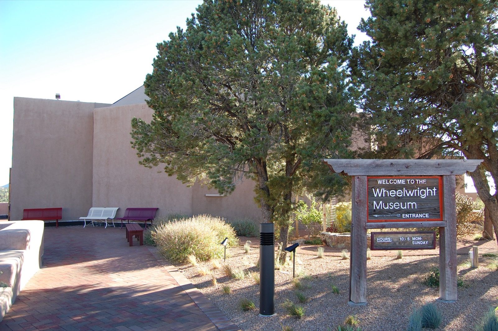 The adobe-style entrance of the Wheelwright Museum of the American Indian in Santa Fe, New Mexico, built in the form of a traditional Navajo hooghan with a rounded doorway and vigas along the roofline.
